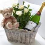 Champagne, bjørn og blomster i en gavekurv